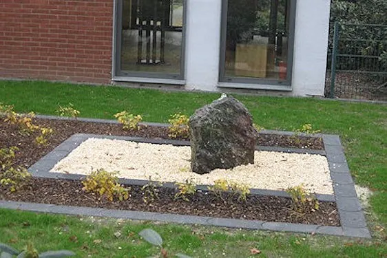 Kleiner Garten vor der Friedhofshalle mit Stein und Rosenbeet